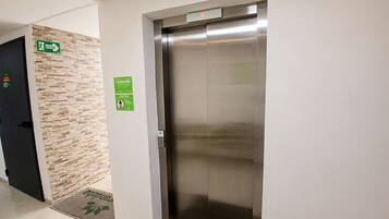 En elevator med et digitalt display, et fastgjort nødudgangsskilt og en dør med et grønt sikkerhedssymbol.