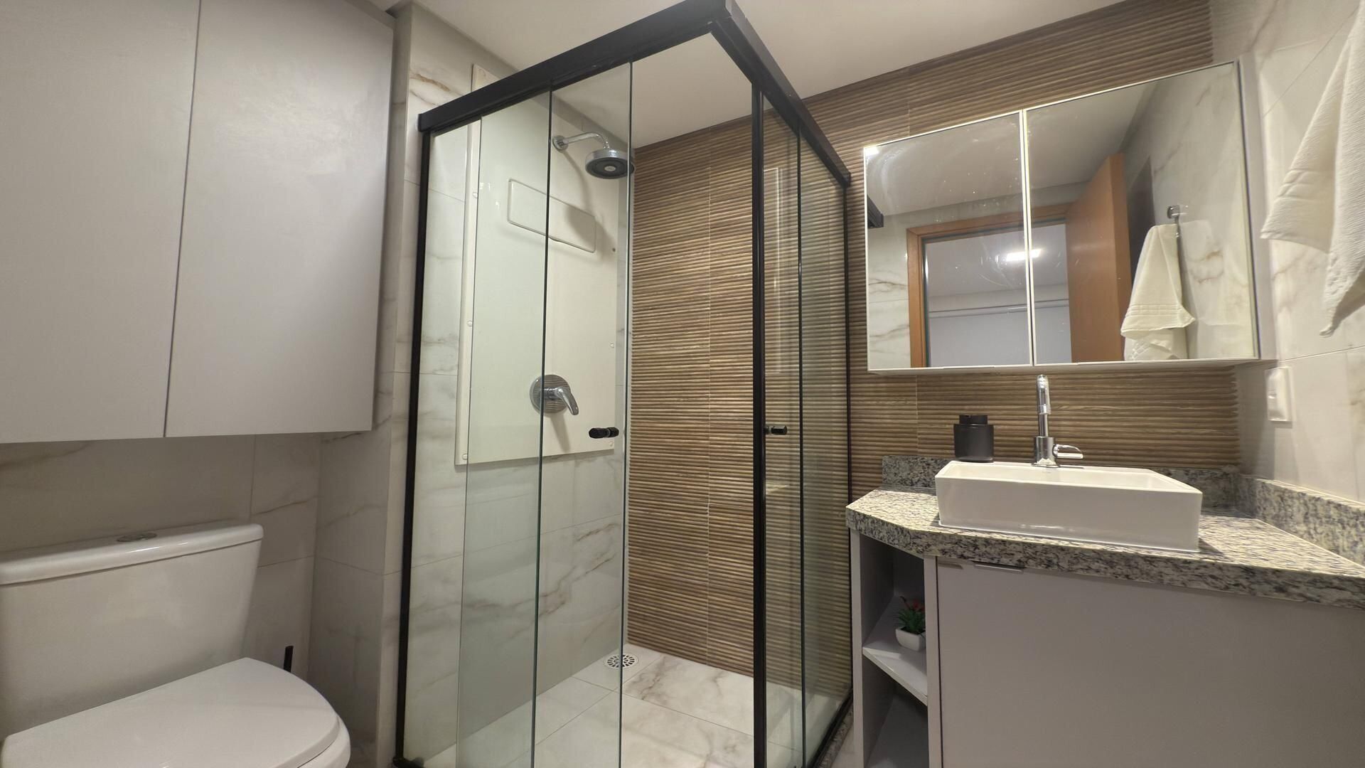 Une salle de bain moderne avec une douche à parois de verre, des toilettes blanches, un sol carrelé en marbre et un lavabo sur un plan de travail en granit.