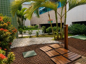 A landscaped outdoor area with a wooden deck, pebbles, and various plants. - 2 bedroom flat close to the Natural Pools (Ipojuca)
