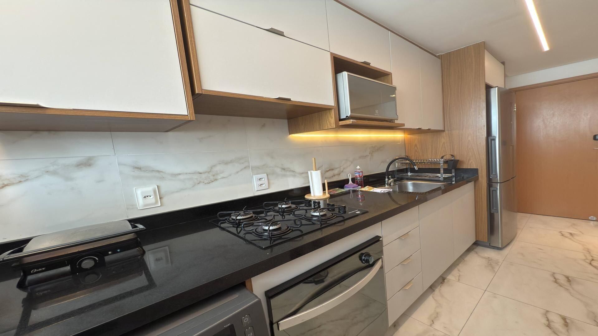 A modern kitchen with a gas stove, oven, stainless steel sink, and wooden cabinets.