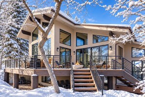 A modern multi-story house with a deck, outdoor seating, and a fire feature.