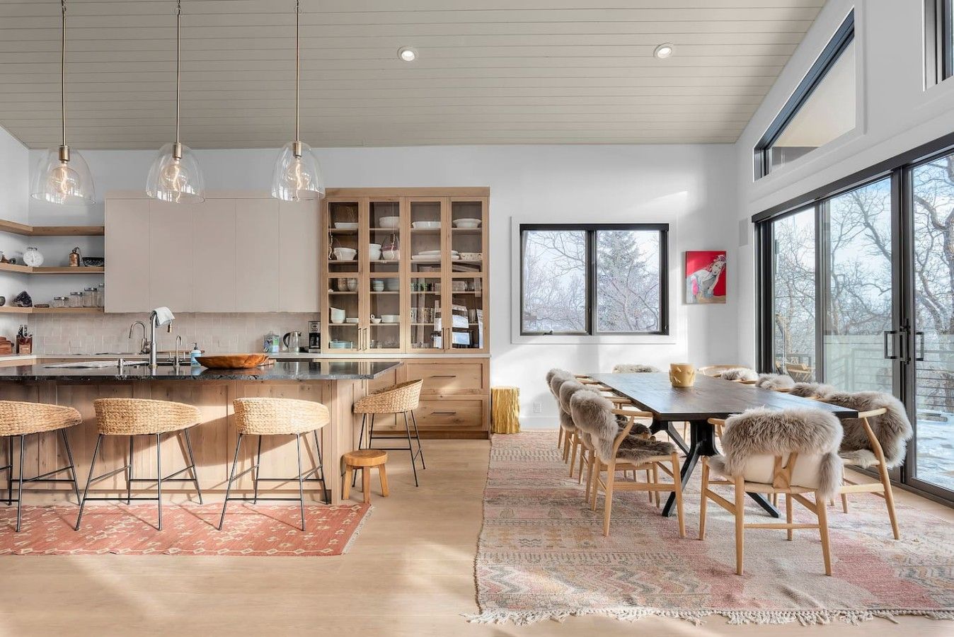 Una cocina moderna con una isla central, taburetes de bar y una zona de comedor con una mesa grande y sillas.
