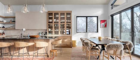 Una cocina moderna con una isla central, taburetes de bar y una zona de comedor con una mesa grande y sillas.