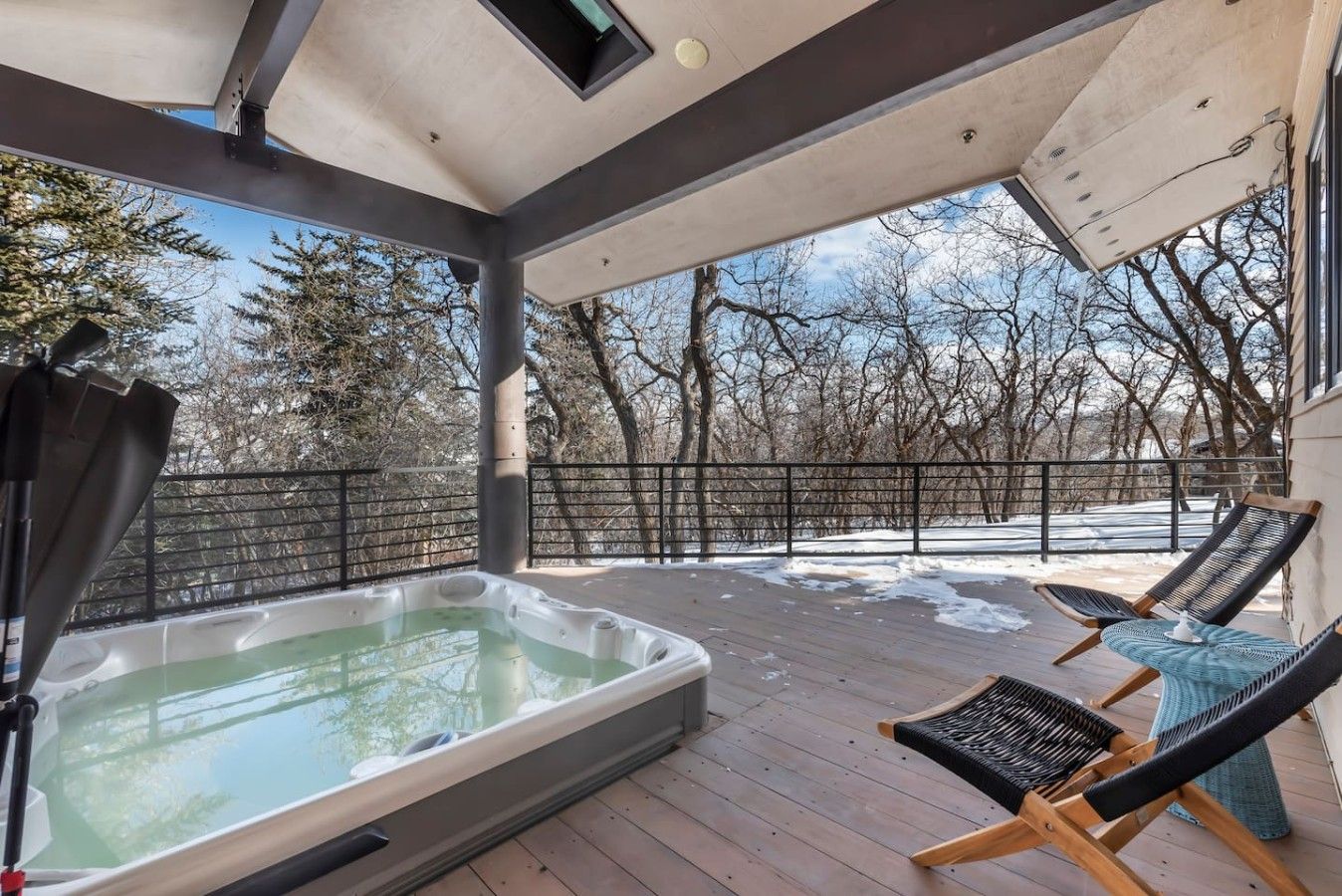 Een overdekt buitengebied met een hottub, twee lounge fauteuils en uitzicht op een besneeerd landschap.