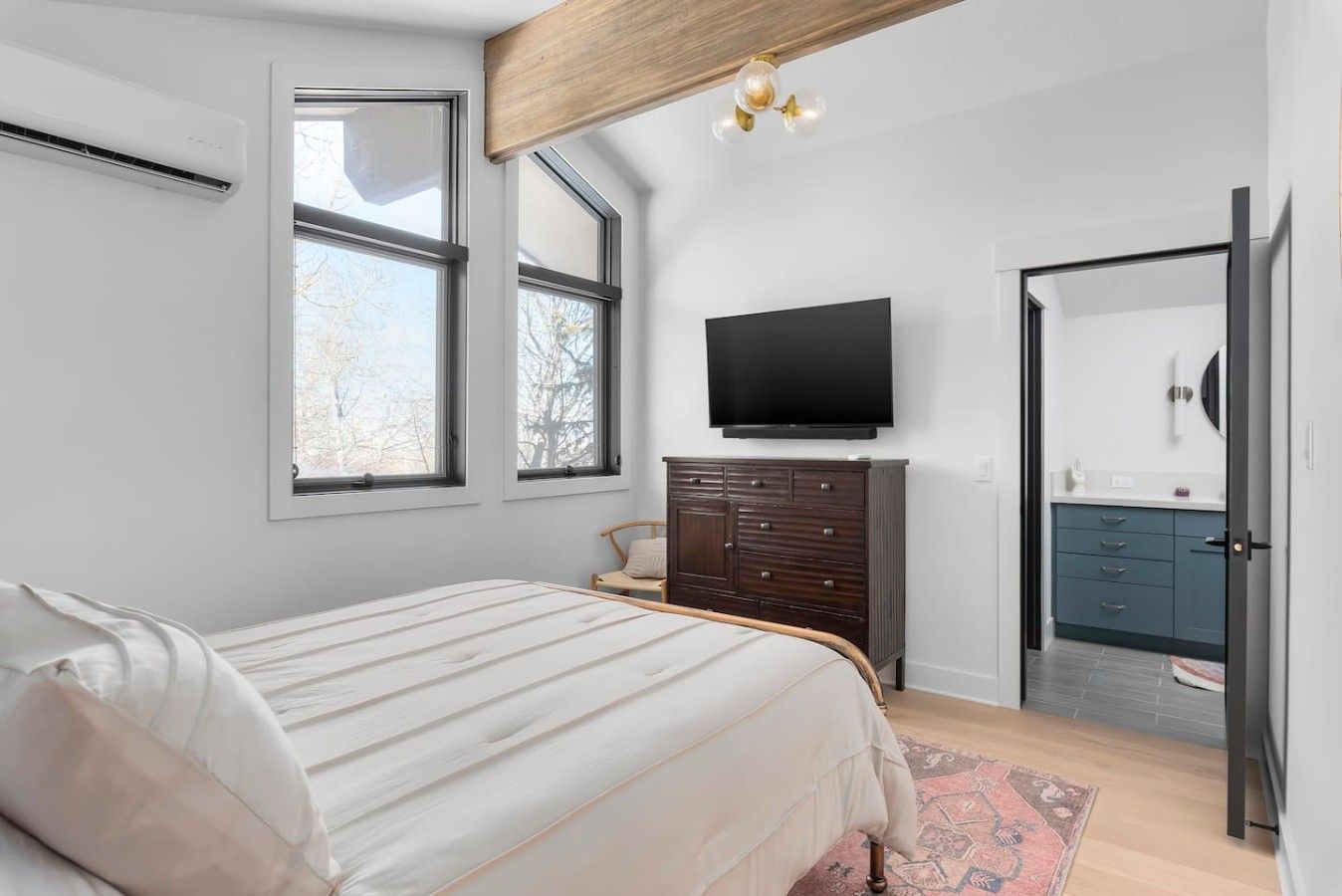 A bedroom with a bed, dresser, TV, and a door leading to a bathroom.