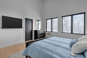 A bedroom with a bed, a dresser, a TV, and windows with a view of trees. - Scenic Alpine Getaway, Hot Tub, Sauna, Views (Park City)
