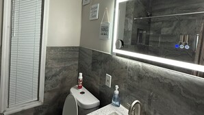 Ein Badezimmer mit Toilette, Waschbecken und Spiegel. Auf dem Waschbecken stehen Flaschen mit Handdesinfektionsmittel.