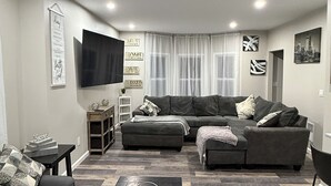 Ein modernes Wohnzimmer mit einem Ecksofa, einem Couchtisch und einem flachbildschirmigen Fernseher an der Wand.
