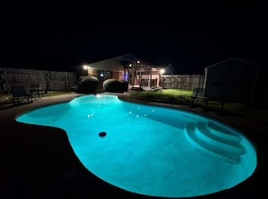 En pool i månskenet, med ett hus och en inglasad uteplats i bakgrunden.