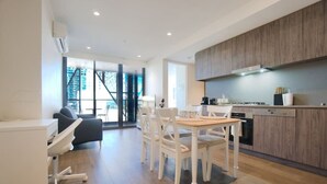 A modern kitchen with wooden cabinets, a dining area with white chairs, and a large window providing a view of the outdoors. - Adelaide Central 1BR APT Overlooking Rundle Mall (Adelaide)
