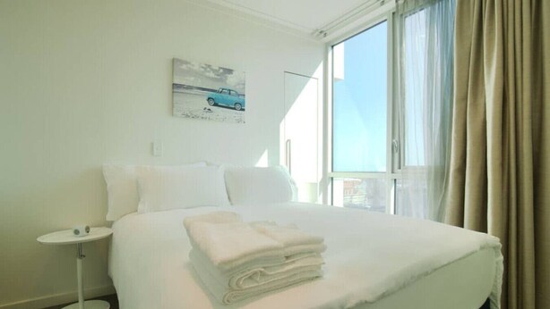 A hotel room with a large bed, a small bedside table, a window with curtains, and a painting on the wall.
