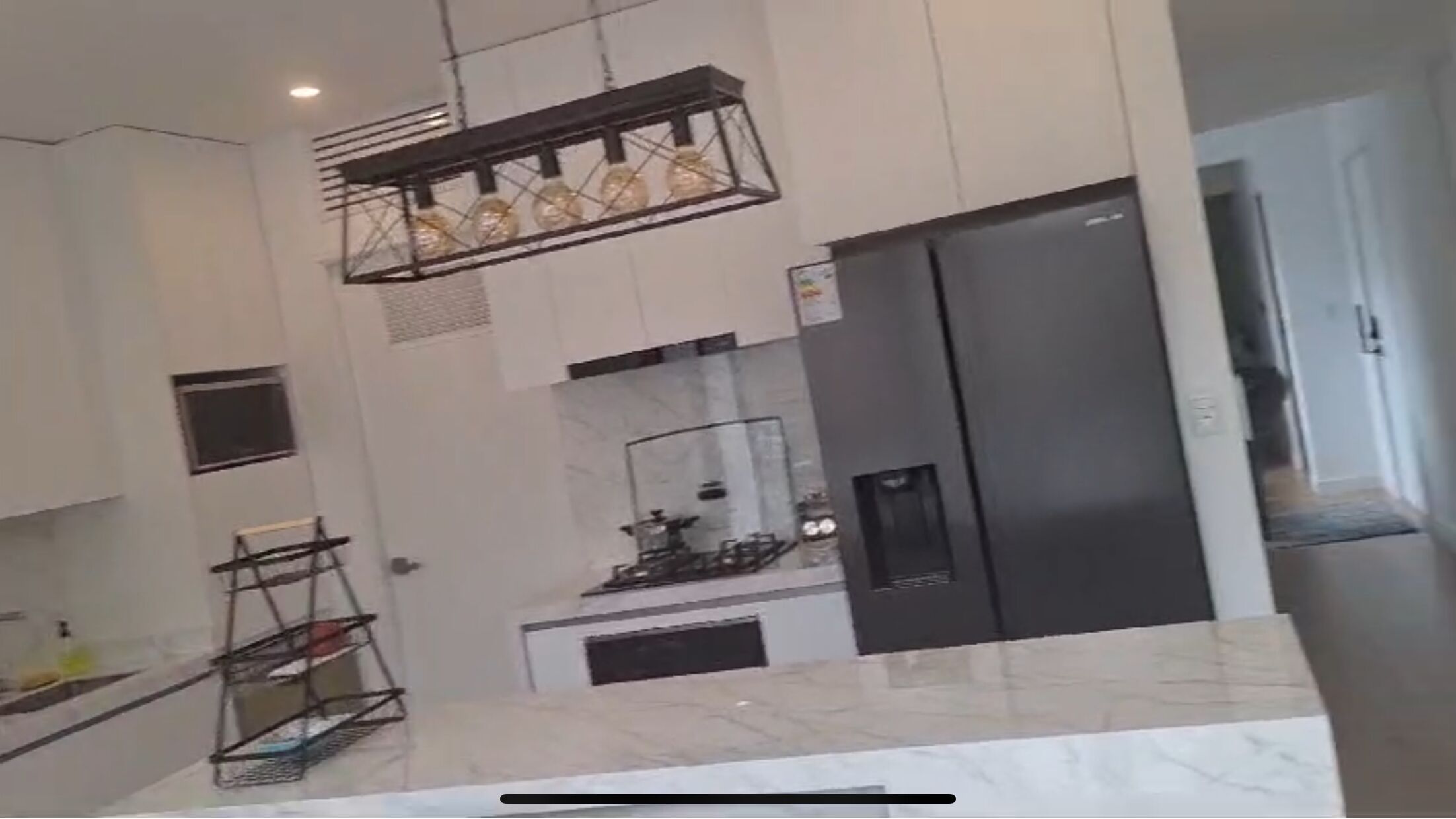 A modern kitchen with a stainless steel refrigerator, a hanging light fixture, and a marble countertop.