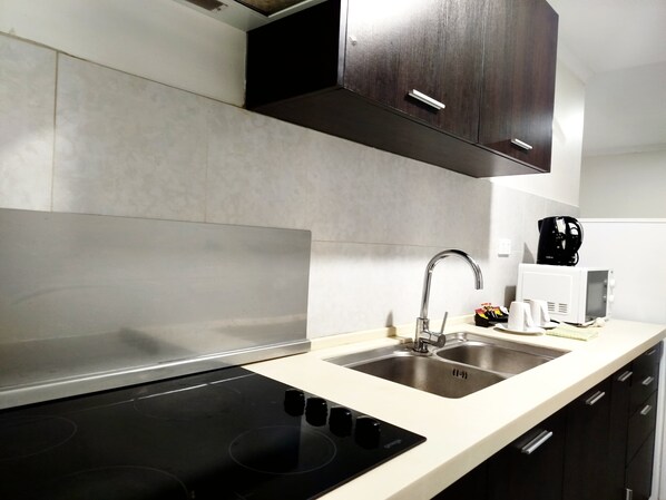 Una cocina moderna con una placa de inducción negra, un lavamanos de acero inoxidable y armarios de madera oscura.