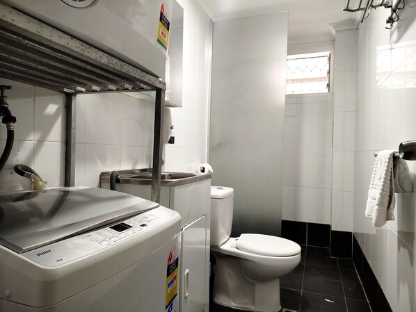 A compact bathroom with a white toilet, a sink, and a Haier washing machine.