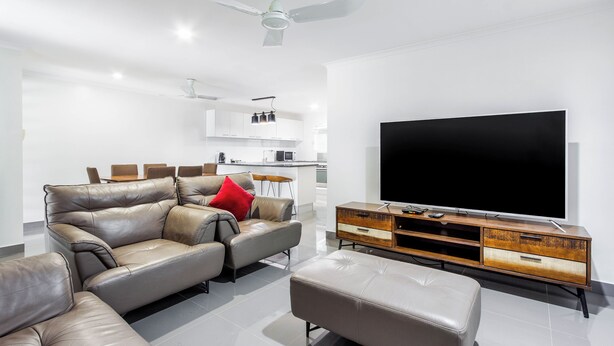 A modern living room with a leather sofa, ottoman, and a wooden entertainment unit with a flat-screen TV. - Citi Serviced Apartments - Gaba Place (Port Moresby)