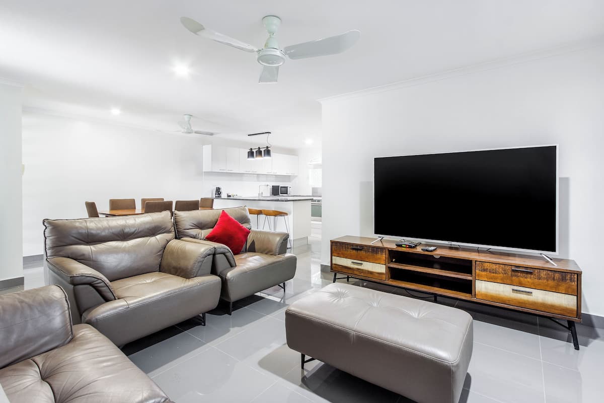 Ein modernes Wohnzimmer mit Ledersofa, Hocker und einer Holz-Unterhaltungsanlage mit Flachbildfernseher.