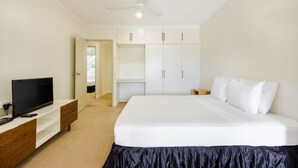 A bedroom with a bed, a TV on a wooden console, a wardrobe, and a ceiling fan. - Citi Serviced Apartments - Gaba Place (Port Moresby)