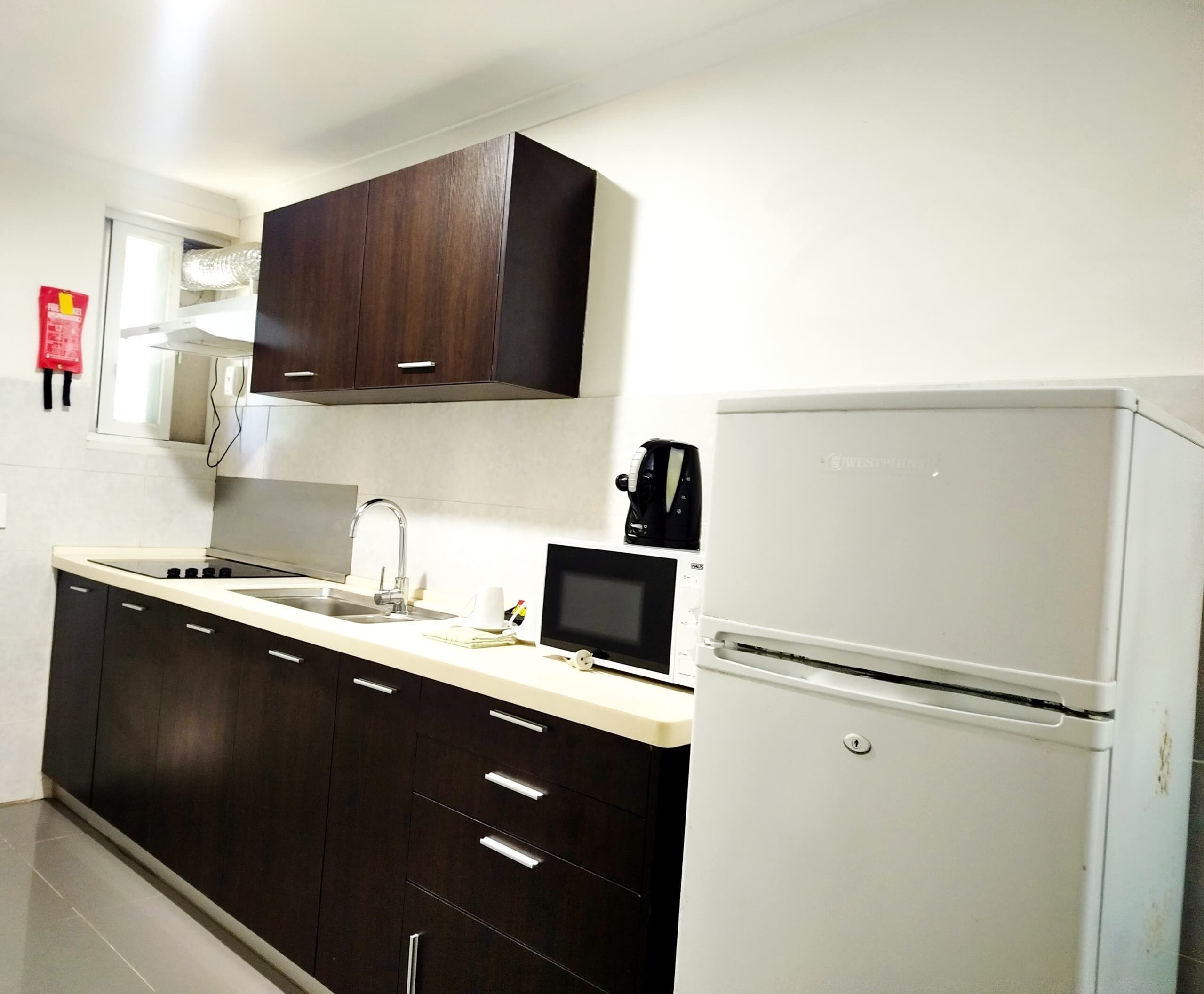 Una cocina con armarios de madera oscura, encimera blanca, estufa integrada, un lavabo y un refrigerador blanco.