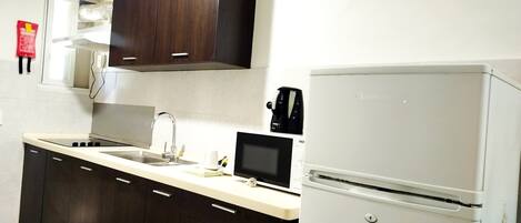Una cocina con armarios de madera oscura, encimera blanca, estufa integrada, un lavabo y un refrigerador blanco.