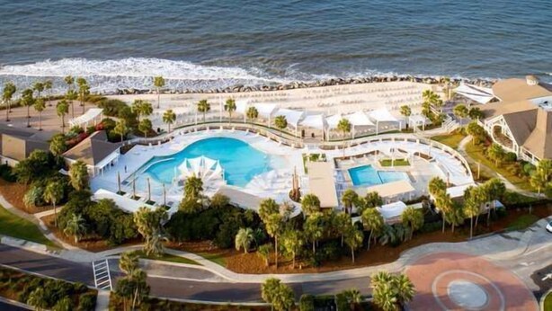 Vista aérea de un resort con una piscina grande, palmeras y una zona de playa.