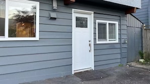 Una casa con una puerta blanca, un ventanal pequeño con persianas y un porche con felpudo.