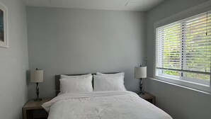 Un dormitorio con una cama, dos mesitas de noche y una ventana con persianas.
