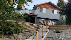 Una escalera con barandales de madera que lleva a una casa con fachada gris y tejado de madera.