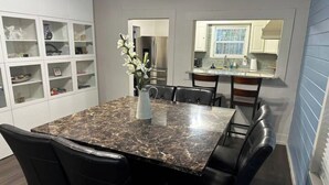 A dining area with a marble table, black chairs, a vase with flowers, and a kitchen in the background. - The Azure Charm — Amazing 3BR 2BA Home 1 Mile to Fort Sam Houston & The Pearl (San Antonio)