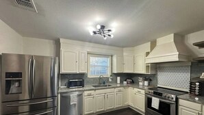 A modern kitchen with white cabinets, stainless steel appliances, a built-in microwave, and a dark wooden floor. - The Azure Charm — Amazing 3BR 2BA Home 1 Mile to Fort Sam Houston & The Pearl (San Antonio)