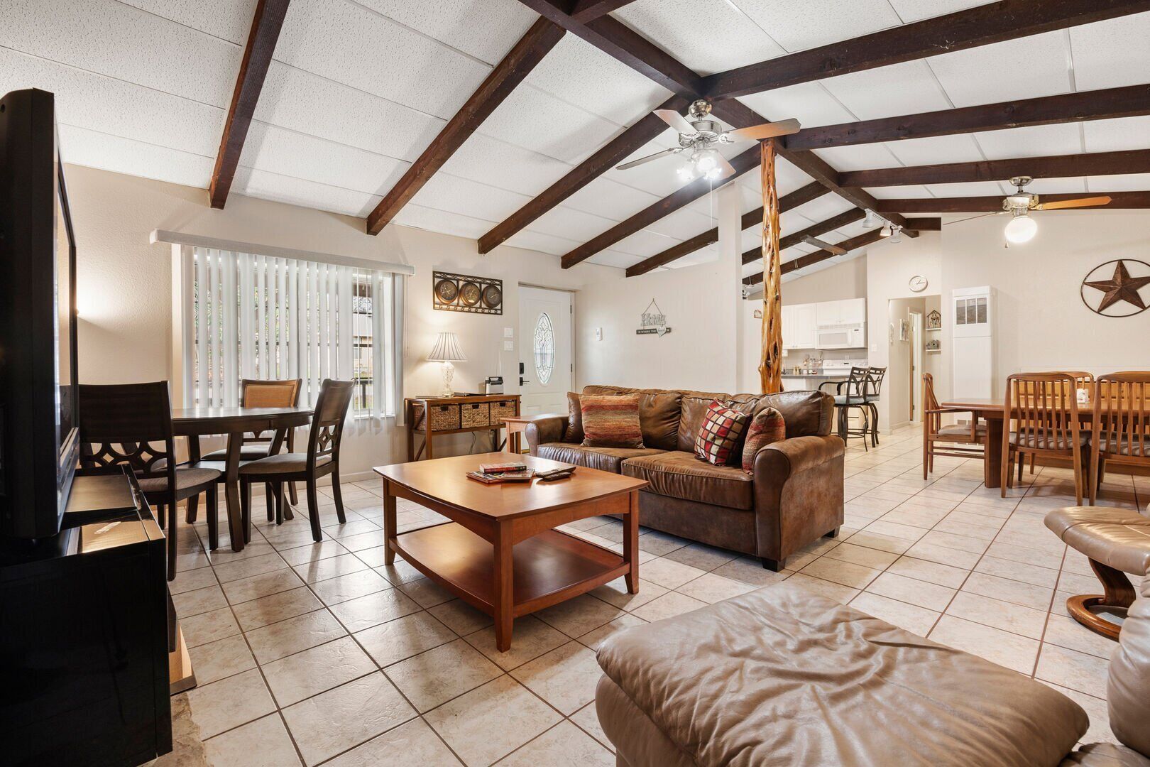A spacious living room with a wooden coffee table, leather sofa, and a dining area with wooden chairs.