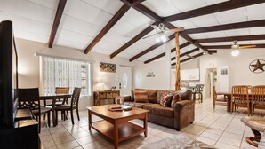 A spacious living room with a wooden coffee table, leather sofa, and a dining area with wooden chairs.