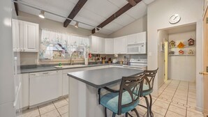 A kitchen with white cabinets, a granite countertop, a built-in island with bar stools, and a clock on the wall.