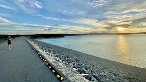 A paved walkway alongside a body of water with a sunset in the background.