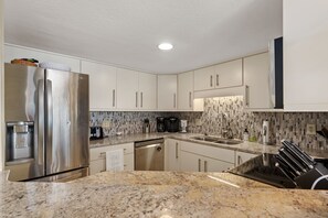 A modern kitchen with stainless steel appliances, granite countertops, and a tiled backsplash. - Sea Rose: Oceanfront Condo, Great Ocean Views, Community Pool (Nags Head)