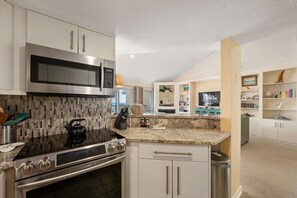 A modern kitchen with stainless steel appliances, a granite countertop, and white cabinetry.