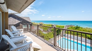 A balcony with white Adirondack chairs, a swimming pool, and a view of the ocean. - Sea Rose: Oceanfront Condo, Great Ocean Views, Community Pool (Nags Head)
