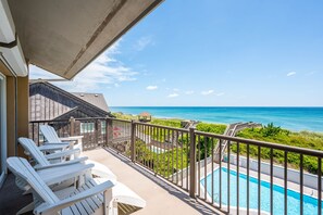 A balcony with white Adirondack chairs, a swimming pool, and a view of the ocean.