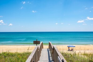 A wooden boardwalk leading to a beach with a clear blue sky and calm sea. - Sea Rose: Oceanfront Condo, Great Ocean Views, Community Pool (Nags Head)