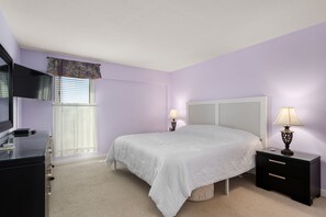 A bedroom with a bed, nightstands, a TV, and a window with curtains.