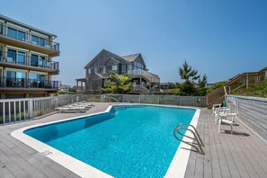 A swimming pool with a wooden deck, lounge chairs, and a stone building in the background.