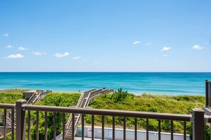 A coastal view with a wooden staircase leading down to the beach, surrounded by greenery.