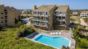 A multi-story hotel with a swimming pool, balconies, and outdoor seating areas. - Sea Rose: Oceanfront Condo, Great Ocean Views, Community Pool (Nags Head)