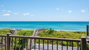 Ein Küstenblick mit einer Holztreppe, die zum Strand führt, umgeben von viel Grün.