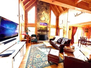 A cozy log cabin interior with a fireplace, a television, and a dining area. - Log Cabin in mountains by Blueridge Parkway, Fenced yard, Private (Marion)