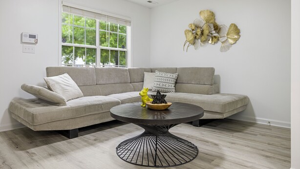 A modern living room with a grey sectional sofa, a round black coffee table, and a decorative gold leaf wall piece. - 13 Minutes from Downtown Raleigh  (Raleigh)