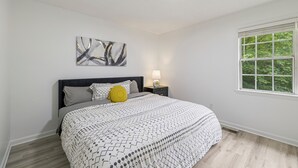 A bedroom with a bed, a nightstand, a lamp, a window, and a wall art piece. - 13 Minutes from Downtown Raleigh  (Raleigh)