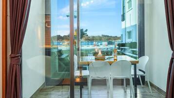 A balcony with a glass door, white plastic chairs, a wooden table, and a bottle of wine.