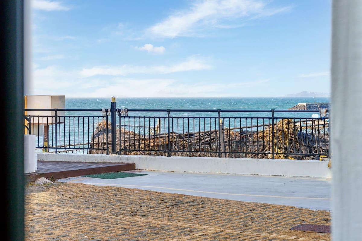 A view from a balcony overlooking a rocky coastline with a metal railing and a clear sky.