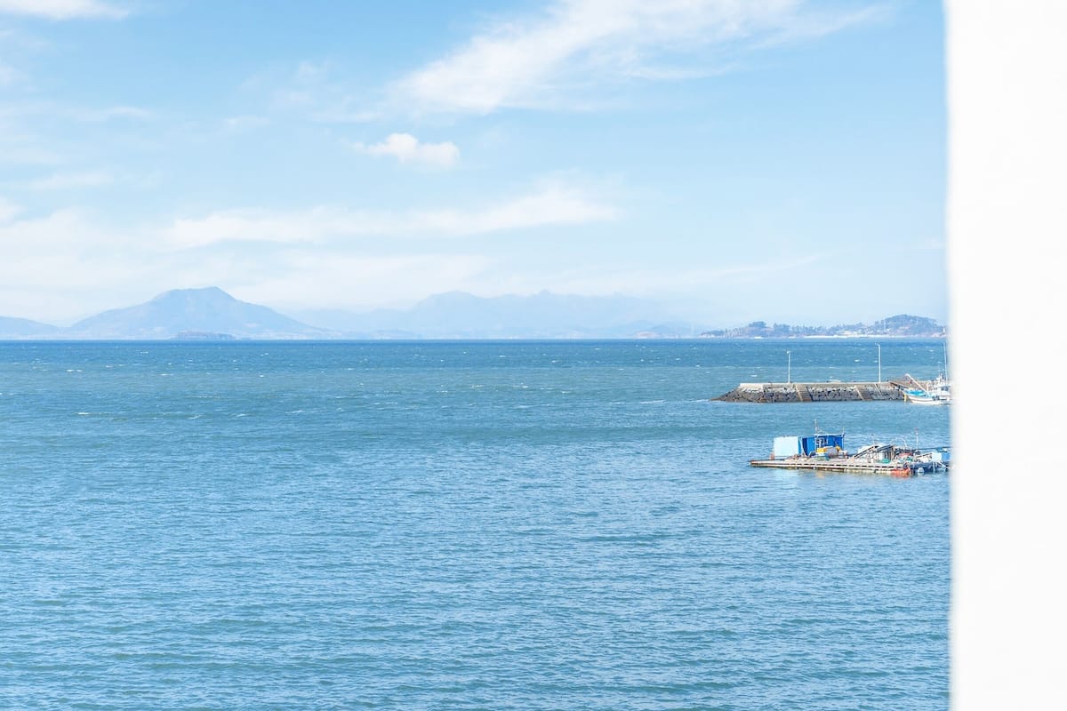 A view of a calm sea with a distant mountain range and a pier with boats.