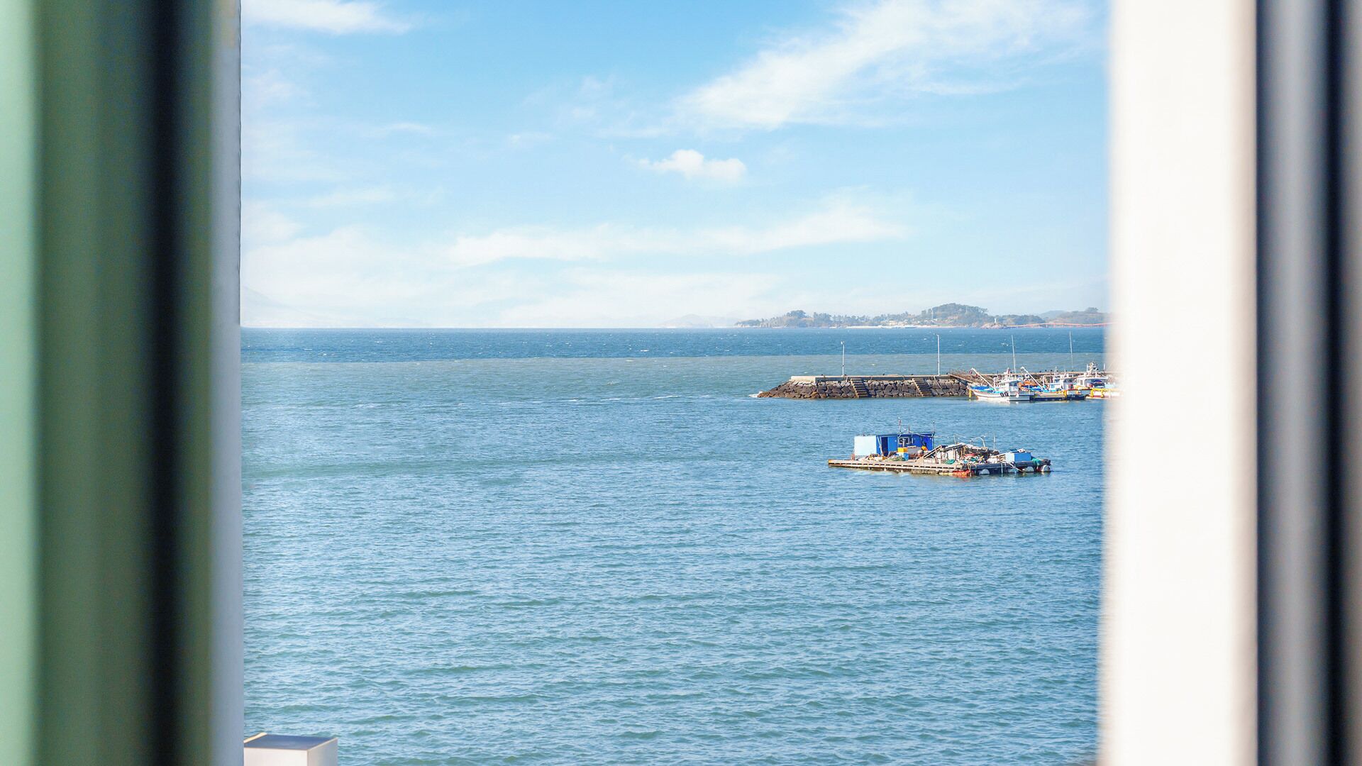 Vista de un mar tranquilo con barcos amarrados en un muelle, cielo despejado y una masa de tierra en la distancia.